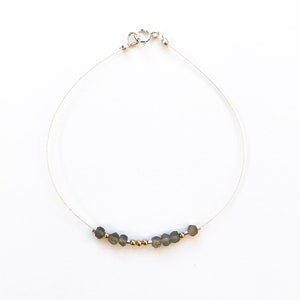 May include: A delicate silver chain bracelet with a row of small, grey gemstone beads and gold beads.
