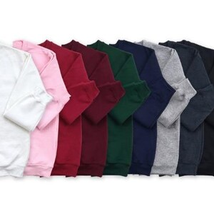 May include: A collection of crew neck sweatshirts in various colors, including white, pink, red, burgundy, green, navy, gray, charcoal, and black. The sweatshirts are neatly folded, showcasing the sleeves and cuffs.