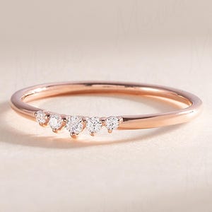 Könnte beinhalten: Ein roségoldener Ring mit einem zarten Band. Der Ring ist mit einer Reihe kleiner, klarer Edelsteine verziert, die in einer sanften Kurve angeordnet sind. Die Edelsteine sind gleichmäßig verteilt und verleihen dem Ring einen dezenten Glanz.
