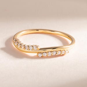 Pode incluir: Um anel dourado com um design de banda dupla. O anel apresenta duas fileiras de pequenas pedras preciosas transparentes, provavelmente diamantes, colocadas ao longo das bandas. O anel &eacute; exibido em uma superf&iacute;cie clara, com sombras suaves.