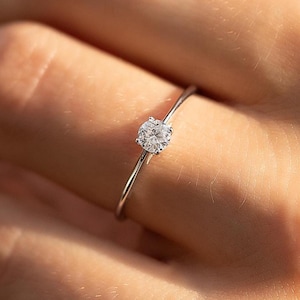 Op de afbeelding: Een delicate zilveren ring met een enkele, rond geslepen diamant. De diamant schittert tegen de eenvoudige band. De ring wordt getoond op een vinger, wat het elegante en minimalistische ontwerp benadrukt. Een klassiek sieraad.