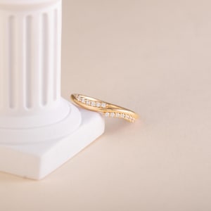Pode incluir: Um anel dourado com um design curvo, adornado com pequenas pedras preciosas brilhantes. O anel &eacute; apresentado sobre um fundo neutro, real&ccedil;ando sua forma elegante e o brilho das pedras. O design do anel &eacute; moderno e sofisticado.