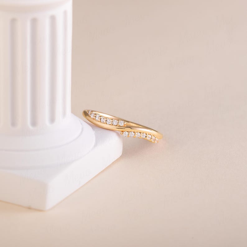 Pode incluir: Um anel dourado com um design curvo, adornado com pequenas pedras preciosas brilhantes. O anel &eacute; apresentado sobre um fundo neutro, real&ccedil;ando sua forma elegante e o brilho das pedras. O design do anel &eacute; moderno e sofisticado.