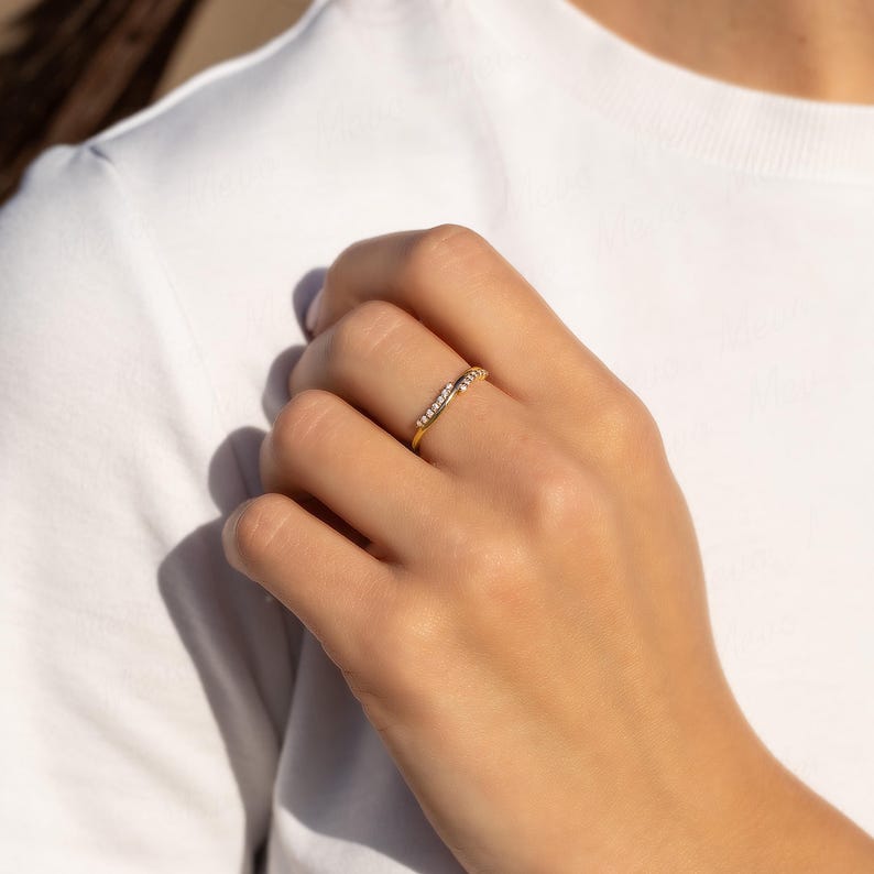 Pode incluir: Um anel dourado com um design curvo, cravejado com pequenas pedras brilhantes. O anel &eacute; usado no dedo de uma pessoa, mostrando seu estilo delicado e elegante. O design do anel &eacute; simples, mas atraente, perfeito para uso di&aacute;rio ou ocasi&otilde;es especiais.