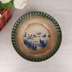 Peut inclure: Un bol en céramique vintage avec un bord vert et un motif bleu et blanc d'oiseaux et de roseaux sur un lac.