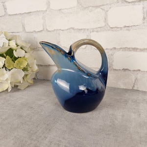 May include: A blue and brown ceramic jug with a wide spout and a rounded body. The jug has a glazed finish and a unique, abstract design.