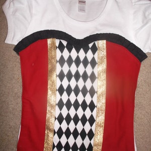 May include: White t-shirt with a red, black, and gold fabric overlay. The overlay has a diamond pattern and gold trim.