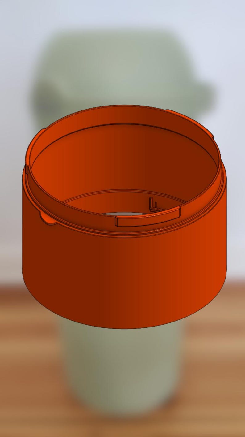 May include: An orange, cylindrical container with a rounded rim and a recessed handle. The container is set against a blurred, light green background, suggesting a product design or prototype.
