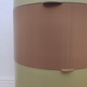 May include: A light green and brown baby diaper pail. The pail has a rounded shape with a brown band around the middle and a curved handle at the top. The brand name "chicco" is visible on the top.