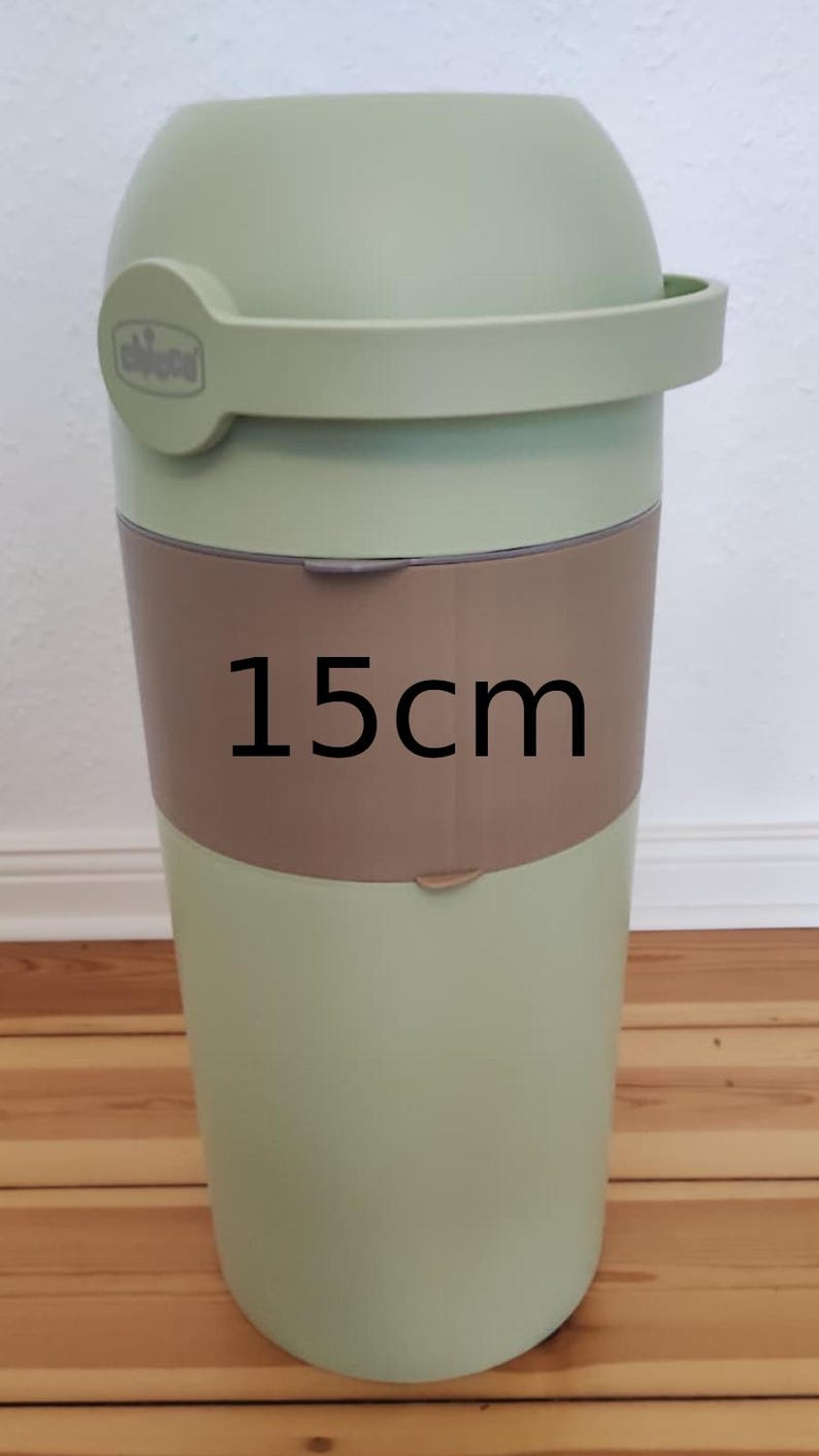 Op de afbeelding: Een lichtgroene luieremmer met een deksel en handvat. De emmer heeft een bruine band in het midden met de tekst "15cm". De emmer is ontworpen om gebruikte luiers in te bewaren en weg te gooien.