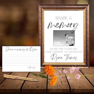 May include: A framed sign with the words "Share a memory" and a photo, alongside a card and pen. The sign includes the text "Please take a card and share a memory of our beloved Ryan Thomas."