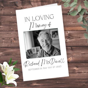 May include: A white memorial card featuring the text "IN LOVING Memory of" above a black and white photograph of a smiling man. The name "Richard McDowell" and dates "SEPTEMBER 18, 1944- MAY 27, 2023" are below the photo.