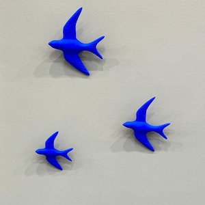 Könnte beinhalten: Ein Set aus drei Keramikbechern mit gesprenkelter, matter Oberfläche. Die Becher sind in Creme-, Hellgrau- und Dunkelgrautönen gehalten. Jeder Becher hat ein schlichtes, minimalistisches Design und einen abgerundeten Henkel.