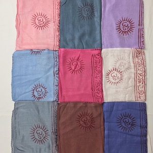 Puede incluir: Una colección de nueve pañuelos rectangulares dispuestos en cuadrícula, cada uno de un color sólido incluyendo rosa, azul, lavanda, gris, magenta, blanco, marrón y morado. Cada pañuelo muestra un símbolo Om rojo oscuro impreso con rayos.
