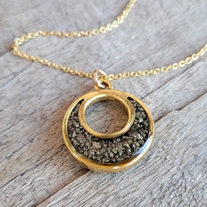 May include: A gold necklace with a round pendant featuring a crescent moon design filled with small, dark gray stones.