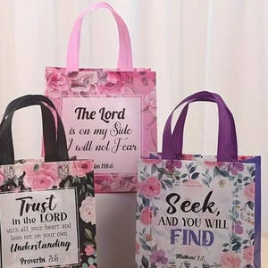 May include: Three reusable tote bags with floral patterns and inspirational quotes. The bags are pink, purple, and black with white lettering. The quotes are "Trust in the Lord with all your heart and lean not on your own understanding Proverbs 3:5", "The Lord is on my side I will not fear Im 118:6", and "Seek, and you will find Matthew 7:7".