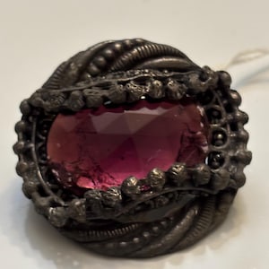 May include: A silver ring with a large, faceted, purple gemstone set in a detailed, ornate design.