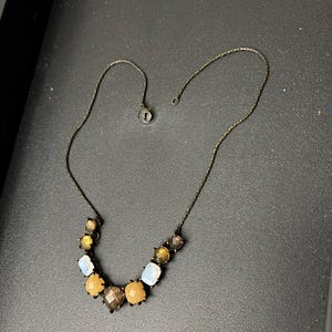 May include: A gold chain necklace with a row of faceted, multi-colored stones. The stones are in shades of brown, yellow, and white.