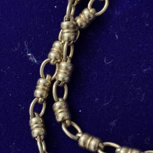 May include: A gold chain necklace with a unique design featuring alternating oval and round links. The chain is made of a smooth, polished metal.