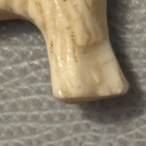 May include: Close-up of a cream-colored ceramic figurine's leg. The leg has a smooth, glossy finish with subtle brown markings and a rounded foot. The figurine appears to be a small animal or creature.