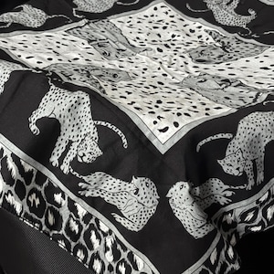 May include: Black and white bandana with a repeating pattern of leopards. The bandana has a white border and a black background.