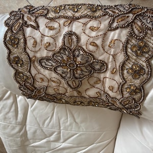 May include: A white couch with a beaded throw pillow featuring a floral design in gold and brown.
