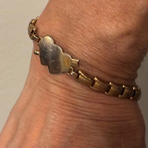 May include: Gold-toned bracelet with a heart-shaped clasp pierced by an arrow. The bracelet features a series of interlocking links. The heart clasp is silver-toned. A piece of jewelry.
