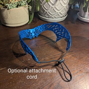 May include: A blue, 3D printed, decorative headband with a delicate, intricate design. The headband has an optional black elastic cord attachment.