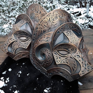May include: Three intricately carved, bronze-colored masks with ornate designs. The masks have a Celtic knotwork pattern and are detailed with gold accents.