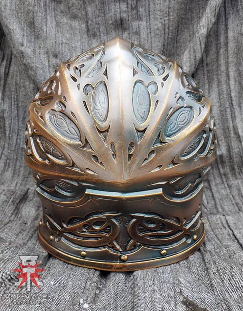 May include: A bronze helmet with intricate, ornate designs. The helmet has a rounded top and a pointed crown. The helmet is decorated with a pattern of swirling lines and shapes.