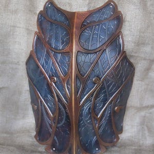 May include: A blue and brown leather armor piece with intricate designs. The armor is made of two pieces that are joined together in the middle. The armor has a decorative pattern of leaves and vines.