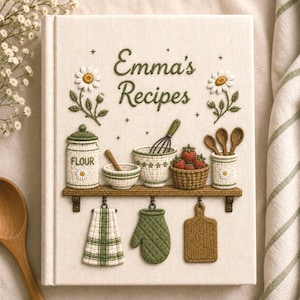 Puede incluir: Un libro de recetas de tela color crema con el texto bordado en verde Emma's Recipes. La portada muestra un estante con un tarro de harina, un bol, un batidor, fresas, cucharas, un paño a cuadros, un guante de cocina y una tabla de cortar.