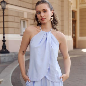 May include: A light blue linen halter top and matching shorts set. The top has a draped design, and the shorts have pockets. The outfit is made of a soft, lightweight fabric, perfect for warm weather. The model is wearing star-shaped earrings.