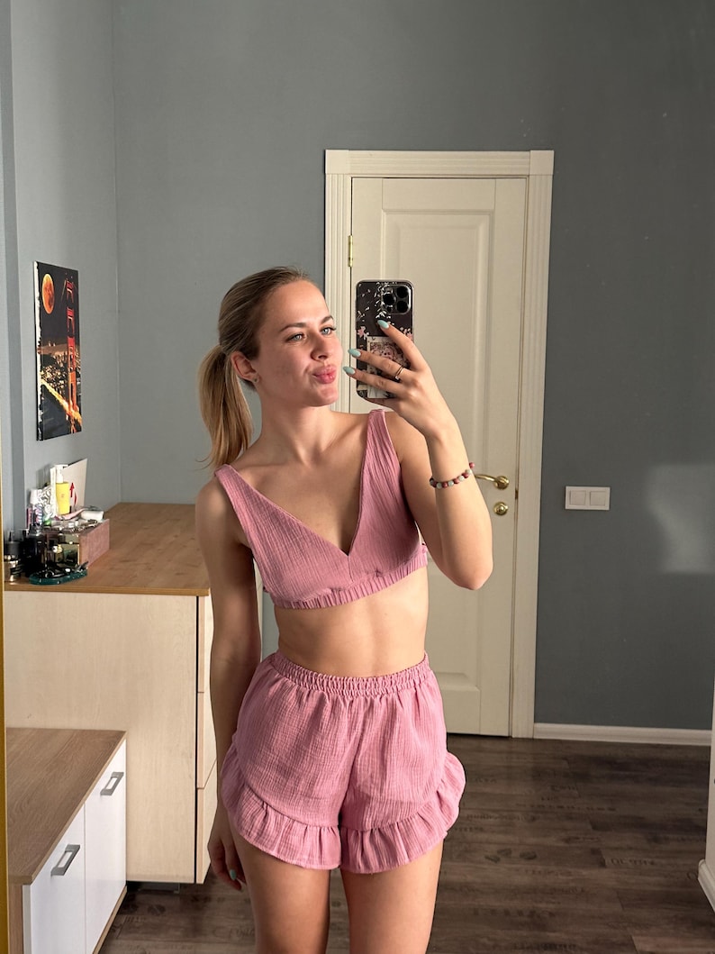 May include: A two-piece set in a dusty rose color, featuring a V-neck crop top and ruffled shorts. The fabric has a textured, crinkled appearance. The outfit is designed for comfort and casual wear.