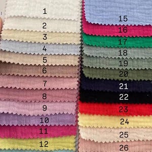 Op de afbeelding: Een kleurenpalet met 28 stofstalen in verschillende kleuren. De stalen zijn genummerd en gerangschikt in rijen. Kleuren zijn onder meer wit, beige, roze, blauw, groen en geel. De stof heeft een getextureerde uitstraling.
