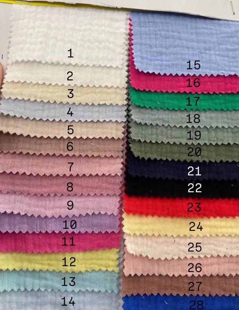 Op de afbeelding: Een kleurenpalet met 28 stofstalen in verschillende kleuren. De stalen zijn genummerd en gerangschikt in rijen. Kleuren zijn onder meer wit, beige, roze, blauw, groen en geel. De stof heeft een getextureerde uitstraling.