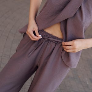 May include: A two-piece mauve outfit. The top is a draped halter style, and the pants have a drawstring waist. The fabric has a subtle texture. The outfit is suitable for casual or semi-formal wear.