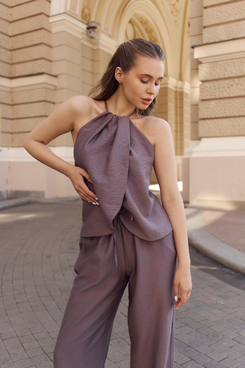 May include: A mauve halter top and matching pants set. The top has a gathered neckline and a tie closure. The pants are wide-legged with a drawstring waist. The outfit is made of a textured fabric and is suitable for casual or semi-formal wear.