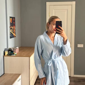 May include: A light blue robe with long sleeves and a tie waist. The robe is made of a textured fabric and has a relaxed fit. The robe is knee-length and has pockets.