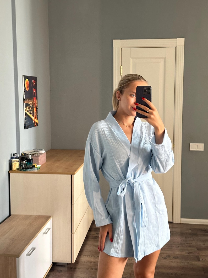 May include: A light blue robe with long sleeves and a tie waist. The robe is made of a textured fabric and has a relaxed fit. The robe is knee-length and has pockets.
