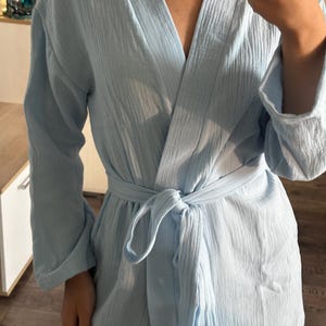 May include: A light blue robe with a textured, crinkled fabric. The robe has long sleeves and a tie belt at the waist. The neckline is a V-shape. The robe is made of a lightweight material.