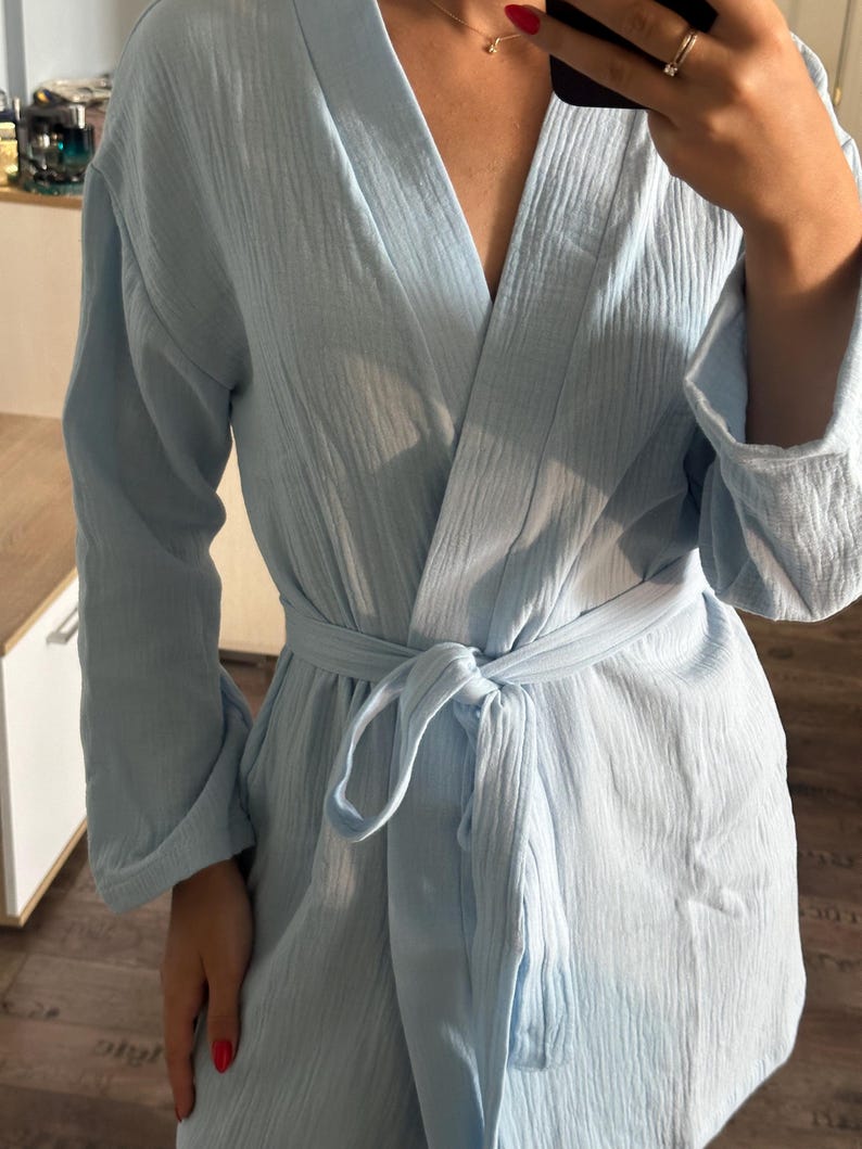 May include: A light blue robe with a textured, crinkled fabric. The robe has long sleeves and a tie belt at the waist. The neckline is a V-shape. The robe is made of a lightweight material.