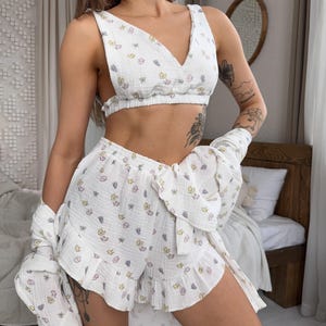 May include: A white pajama set with a floral print. The top is a cropped tank top with a V-neck and the shorts have a ruffled hem.