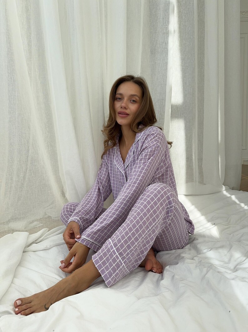 May include: A woman wearing a purple and white checkered pajama set with white piping. The pajamas have long sleeves and long pants.