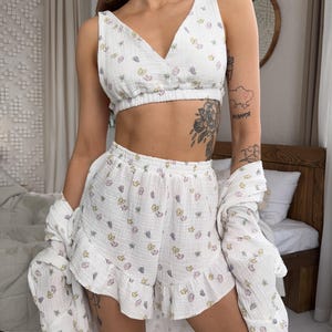 May include: White pajama set with a butterfly print. The set includes a V-neck crop top, ruffled shorts, and a long-sleeved shirt. The fabric appears to be a lightweight, textured material. The butterflies are in pastel colors.