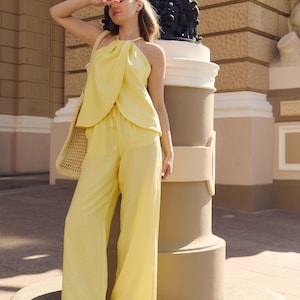 May include: A woman's yellow halter top and wide-leg pants set. The outfit is paired with brown sandals and a woven tote bag. The ensemble is made of a lightweight fabric, perfect for warm weather.
