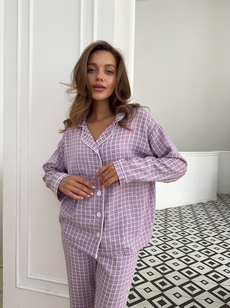 May include: A lavender pajama set with a white checkered pattern and white piping. The top has a button-up front and long sleeves. The pants have a straight leg.