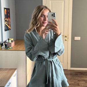 May include: A light teal-colored robe with a ruffled hem and wide sleeves. The robe is tied at the waist with a matching belt. The fabric appears to be a lightweight, textured material. The robe is knee-length.