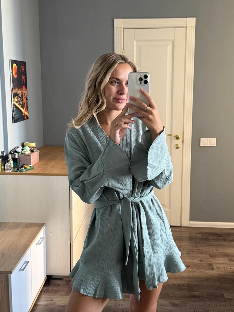 May include: A light teal-colored robe with a ruffled hem and wide sleeves. The robe is tied at the waist with a matching belt. The fabric appears to be a lightweight, textured material. The robe is knee-length.