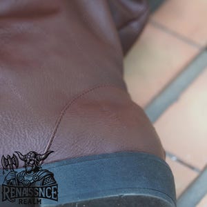 May include: Close-up of the bottom of a brown leather boot with a black rubber sole. The boot has a seam running along the back of the heel.